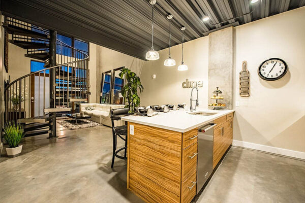 Apartment kitchen with concrete floor, wood style cabinets, and stainless steel appliances.